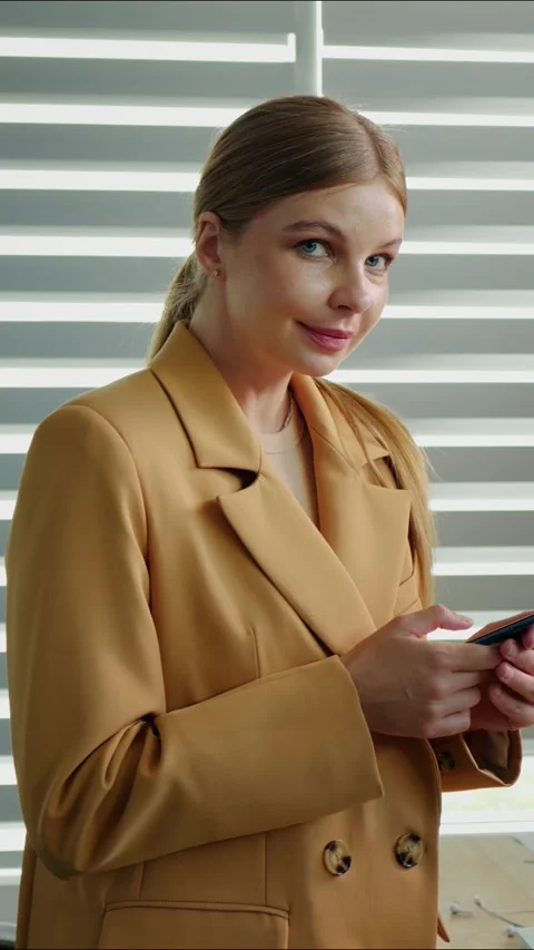 Vertical Screen Portrait Woman using mobile phone then looking in camera. Video stock 299983489