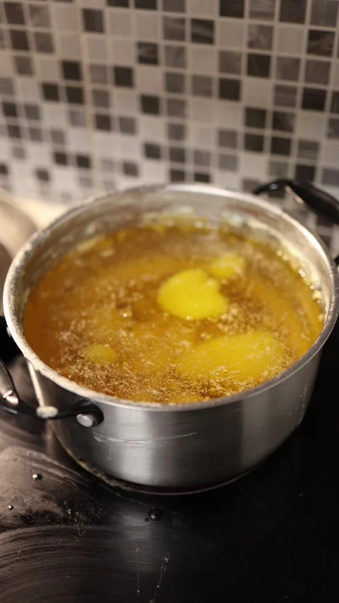 Vertical screen pot of bubbling golden butter during ghee preparation showing ri Stock Footage 319242605