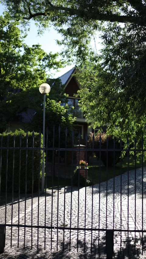 Vertical screen private house hidden behind iron fence surrounded by lush green  Stock Footage 312334735