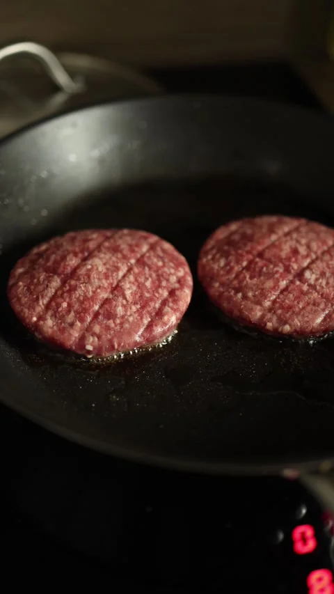 Vertical screen raw beef patties sizzle on hot frying pan with oil drops creatin Stock Footage 318220134