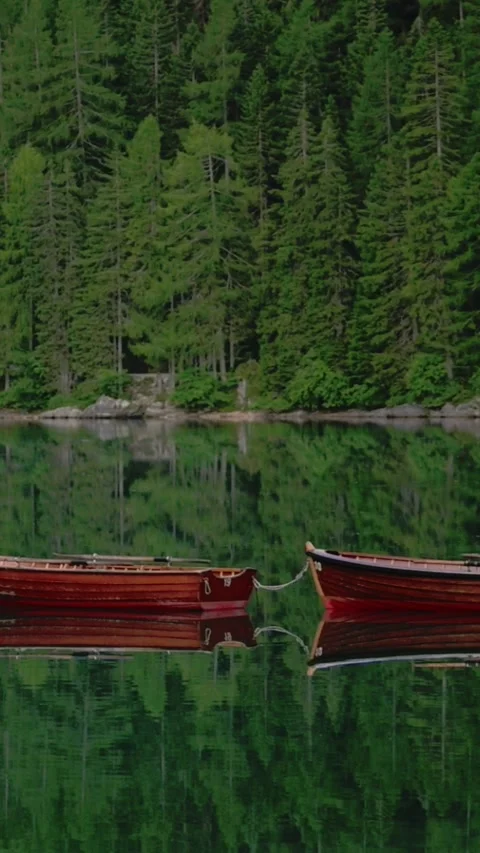 Vertical screen of red boats floating on Lago di Braies with forest reflection Видео 318195478