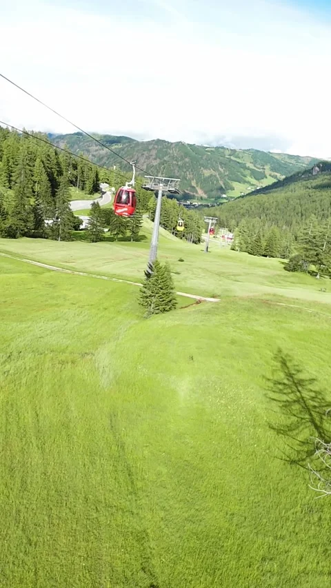 Vertical screen red gondola cabin over green meadow with visible cable and pylon Видео 323149046