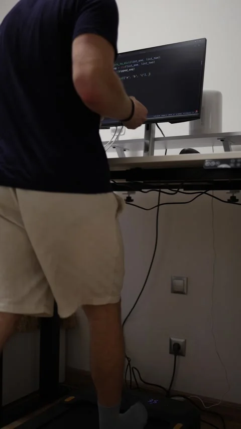 Vertical screen remote IT worker codes from home while walking on a treadmill Stock Footage 346881613