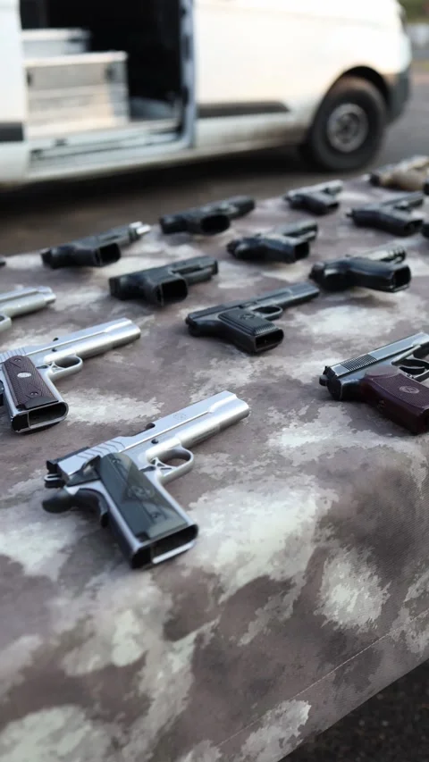 Vertical screen seized handguns displayed on a camo table near an open  Stock Footage 321650786