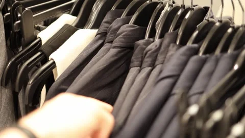 Vertical screen shopper hand browsing elegant black suits on hangers in modern c Video stock 317506970