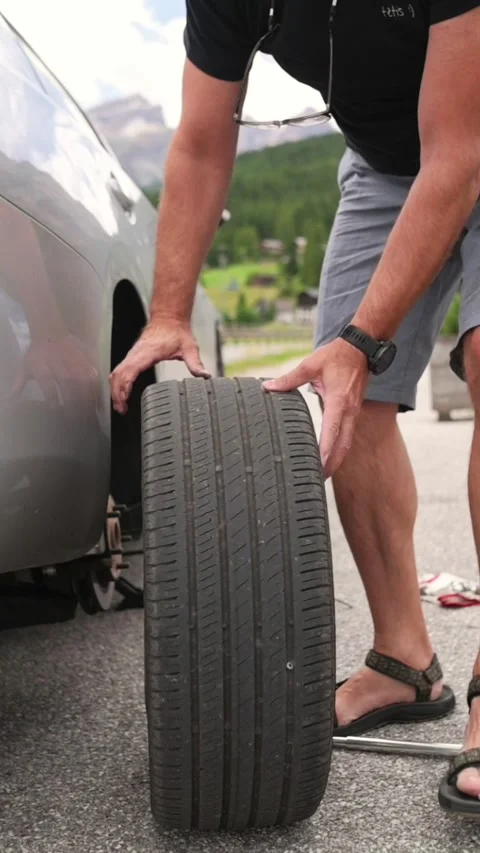 Vertical screen showing man removing worn tire from car during roadside Stock Footage 318195198
