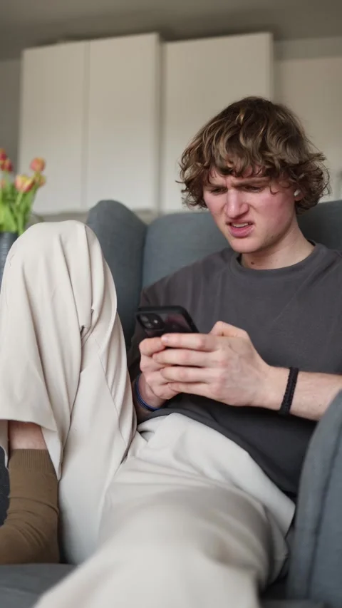 Vertical screen showing a young man sitting in a chair, intently looking at his  Stock Footage 302632606