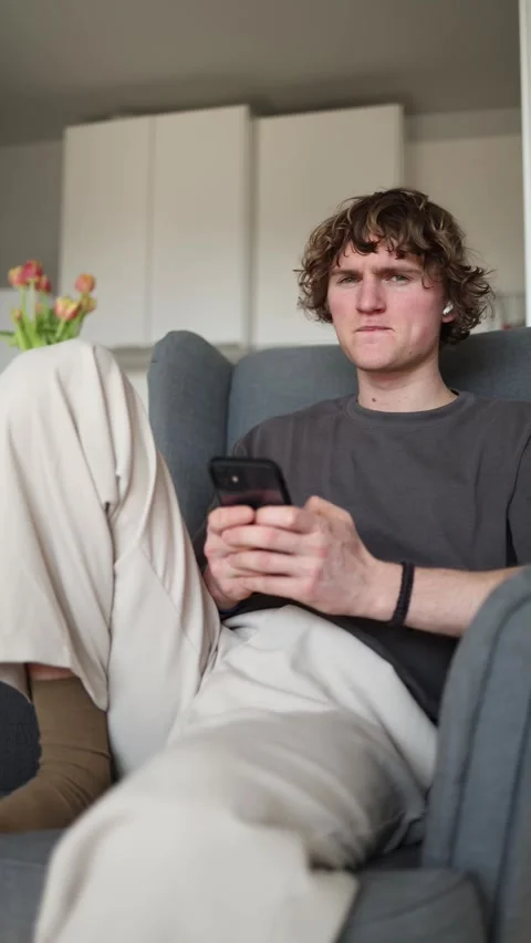 Vertical screen showing a young man sitting on a chair, focused and looking at h Stock Footage 302632623