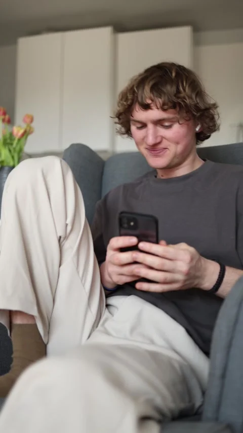 Vertical screen showing a young man sitting comfortably in an armchair, smiling  Stock Footage 302632653
