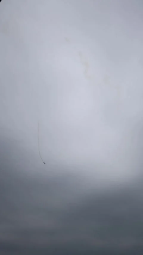 Vertical screen single stunt plane twists through cloudy gray sky leaving faint  Stock Footage 311149954
