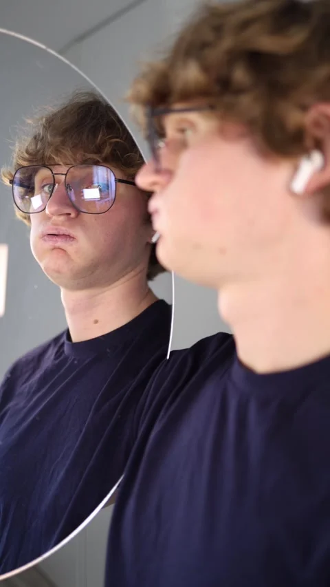 Vertical screen skeptical young man looks at his reflection with a doubtful expr Stock Footage 313268891