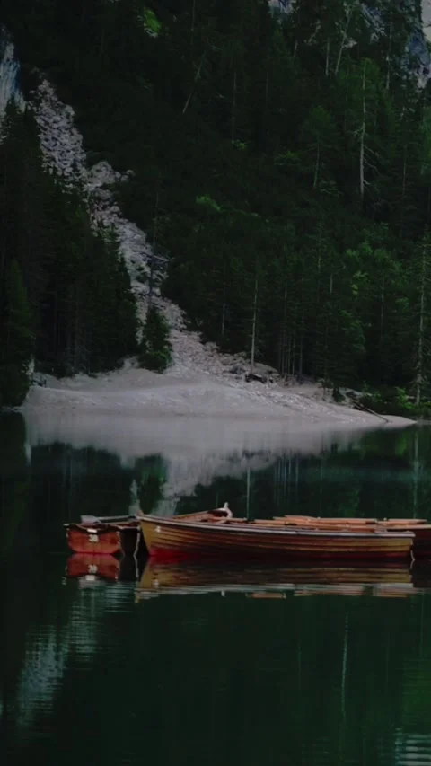 Vertical screen of snowy mountain reflections and red boats on Lago di Braies Stock Footage 318260696