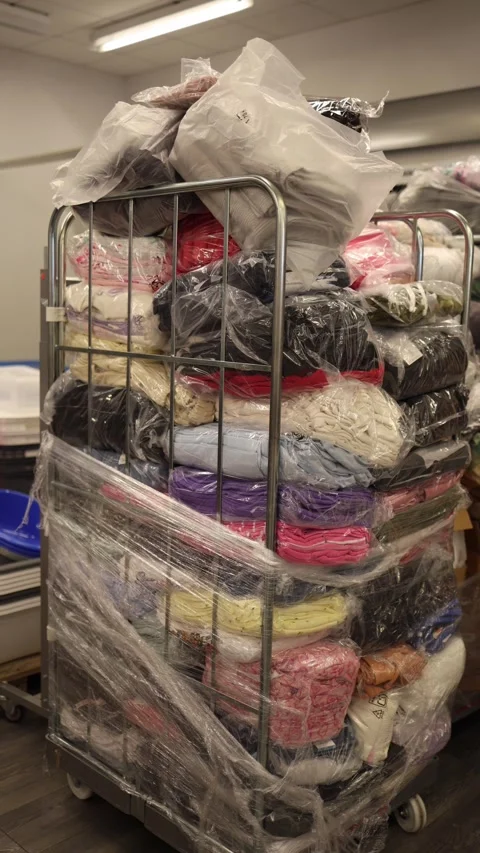 Vertical screen stack of unsold clothing wrapped in plastic on a metal  Stock Footage 330014796