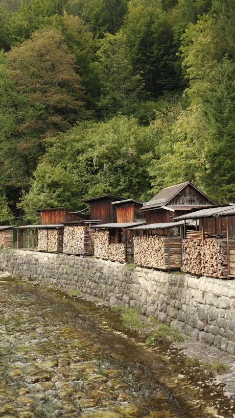 Vertical screen stacked firewood in rustic wooden sheds along a stone wall by a  Stock Footage 318217444