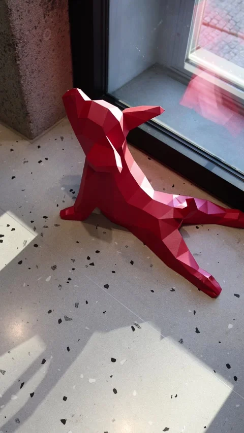 Vertical screen: A striking geometric red dog sculpture sits by the window, bask Stock Footage 304459528