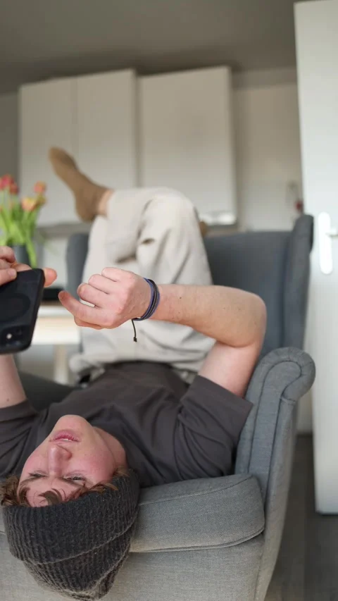 Vertical screen: A student is lying on a chair, engrossed in their phone, which  Video stock 302633315