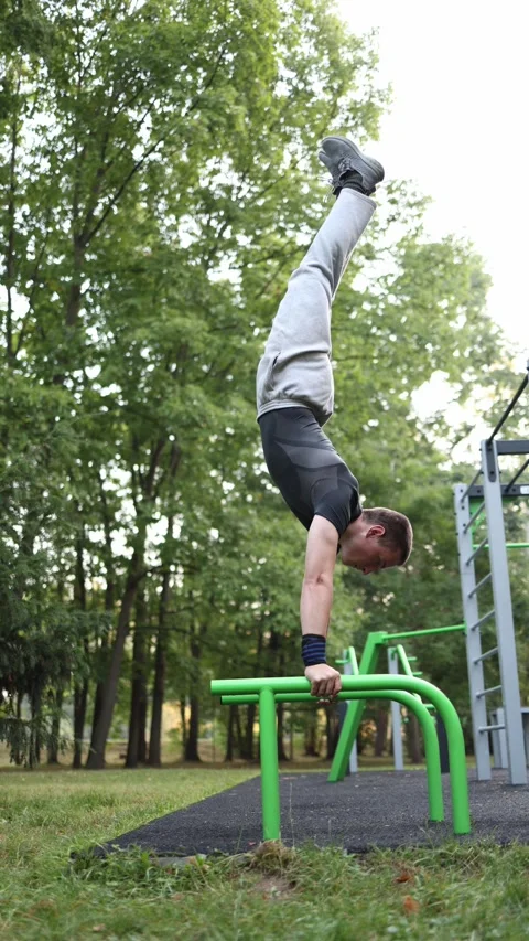 Vertical screen student practices handstand on parallel bars in outdoor park wor Stockbeeldmateriaal 316700735