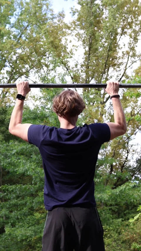 Vertical screen student training outdoors doing pull ups on bar surrounded by gr Stock Footage 315413761