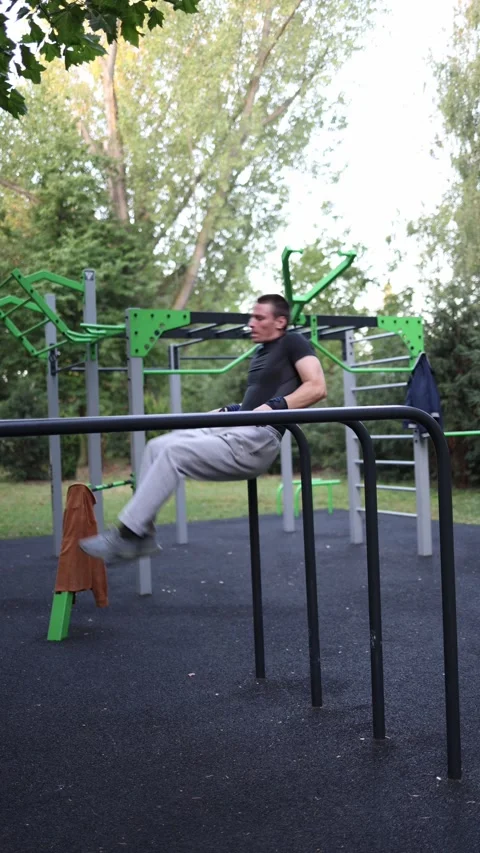 Vertical screen student trains on parallel bars in outdoor gym holding straight  Stockbeeldmateriaal 316700770