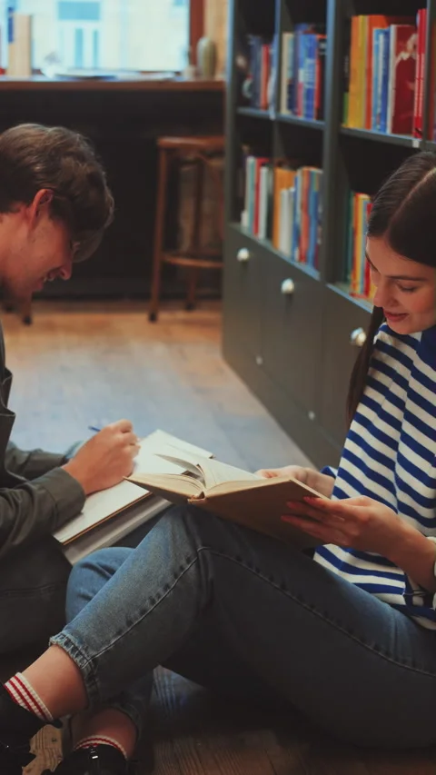 Vertical screen: Students engrossed in reading and discussing book in library Stock Footage 274708566