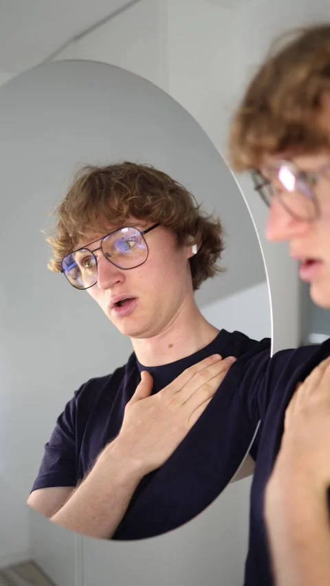 Vertical screen Stunned young man touches his chest while staring at his reflect Stock Footage 313268643