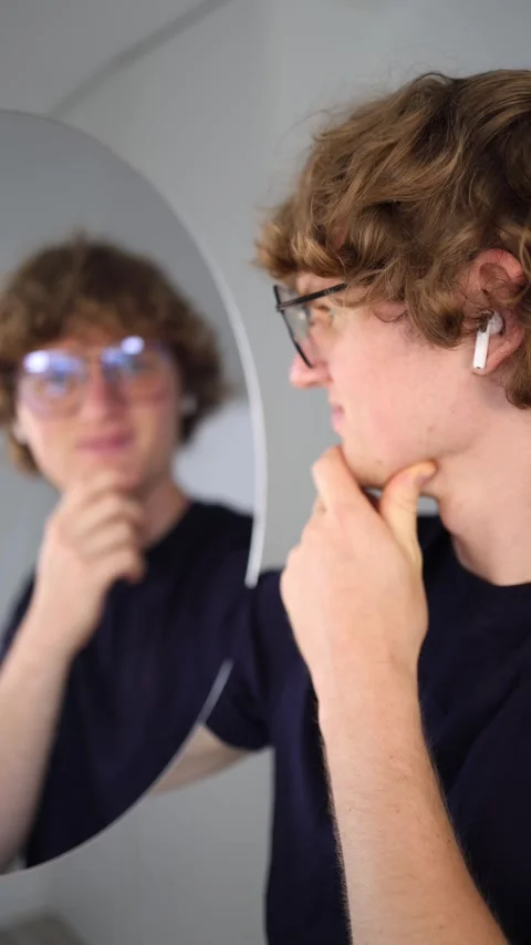 Vertical screen thoughtful young man stares at his reflection while touching his Stock Footage 313268835
