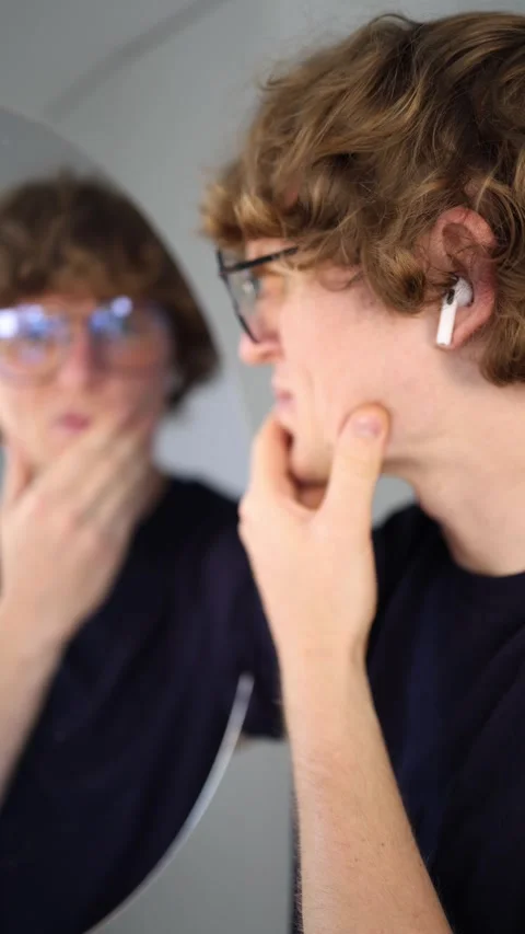 Vertical screen thoughtful young man looks at his reflection with a hand on his  Stock Footage 313268877