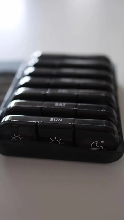 Vertical screen: Three sections of a pill organizer are shown, each marked for m Stock Footage 301240079