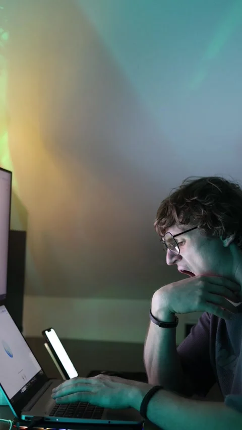Vertical screen tired young man in glasses sitting at desk with laptop and monit Stock Footage 316878079