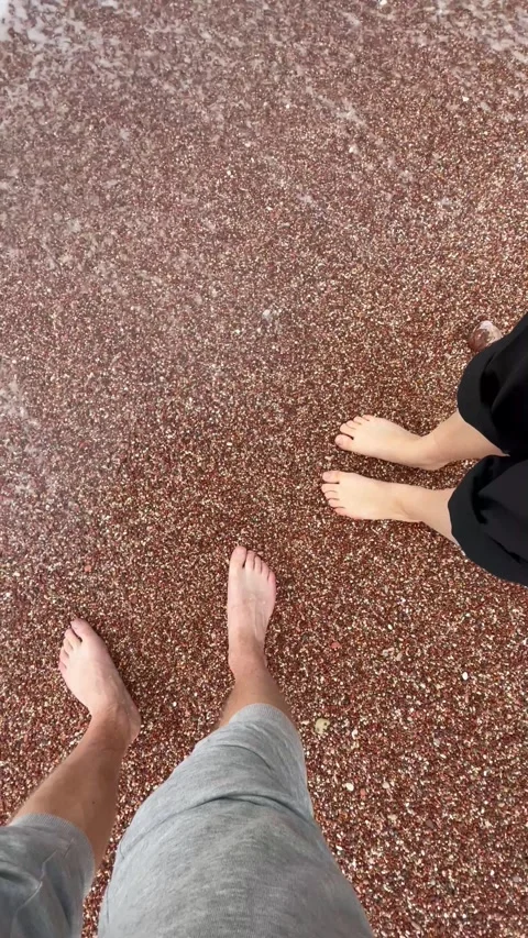 Vertical screen: Two pairs of bare feet standing on a red pebble beach, with gen Stock Footage 296178514