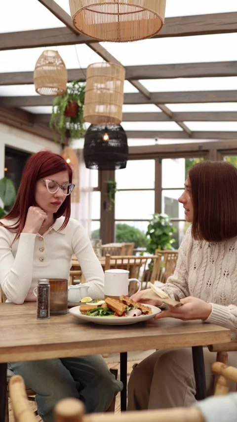 Vertical screen two sisters sit in a cafe as one offers her breakfast  Stock Footage 320827175