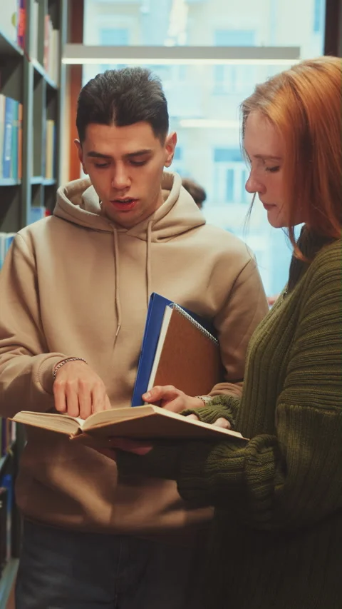Vertical screen: Two students discussing a book in a library aisle Stock Footage 279943025