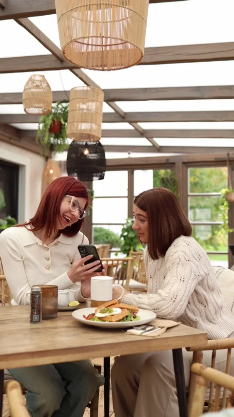 Vertical screen two students sit in a cozy cafe one shows her new boyfriend  Stock Footage 320827193