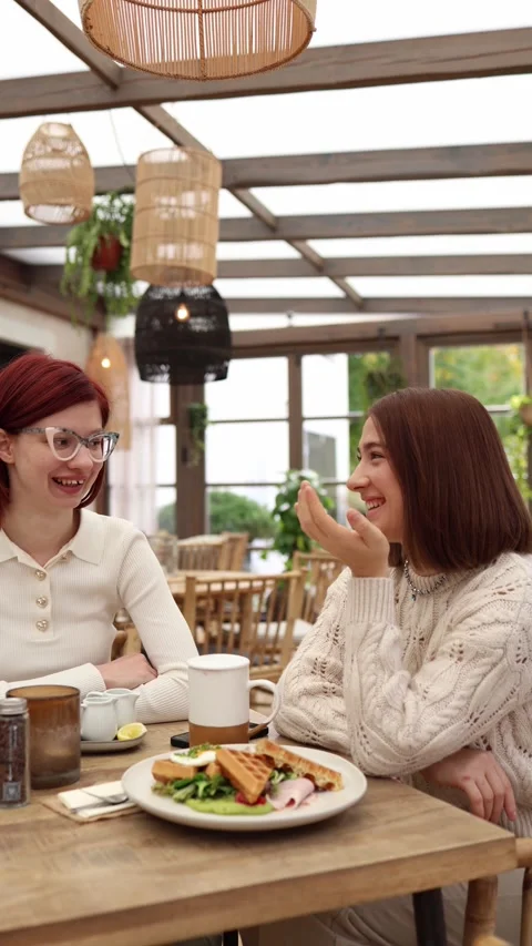 Vertical screen two women sit in a cozy cafe laughing together  Stock Footage 320827172