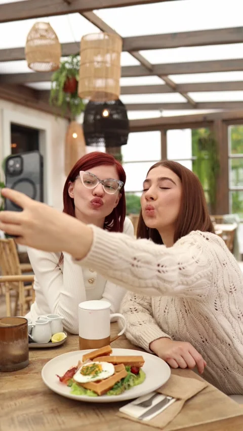 Vertical screen two young bloggers sit in a cozy cafe making duck face selfies  Stock Footage 320827195