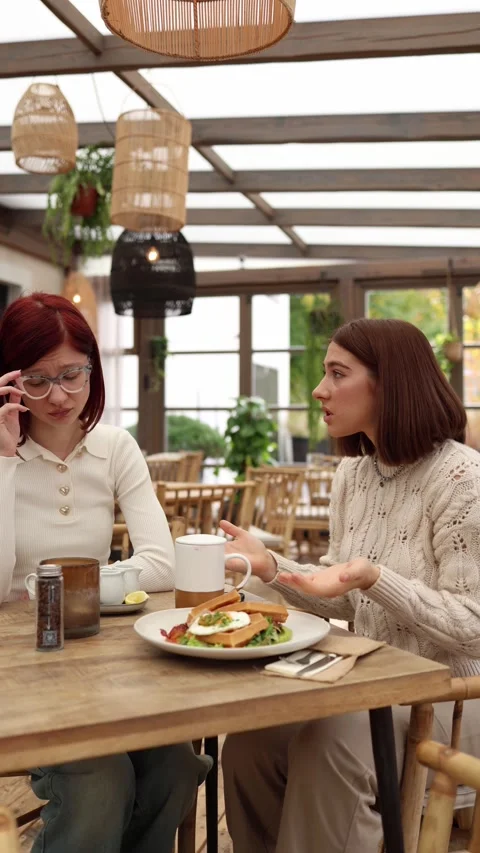 Vertical screen two young women sit in a cafe having a tense argument Stock Footage 320827202