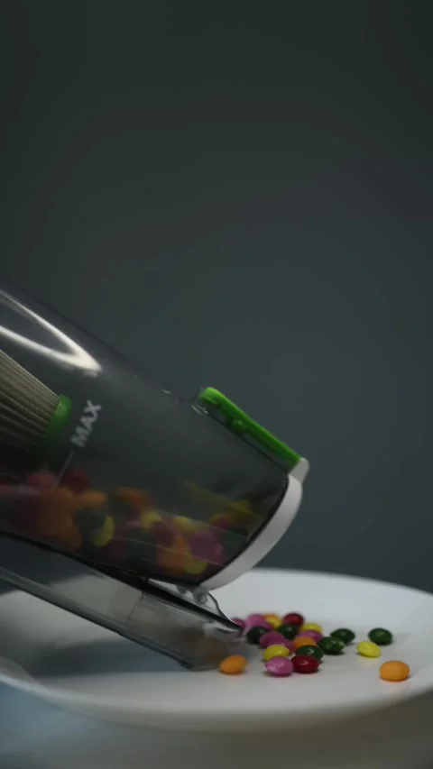 Vertical screen: A vacuum cleaner removes colorful candies from a white plate, s Stock Footage 300021543