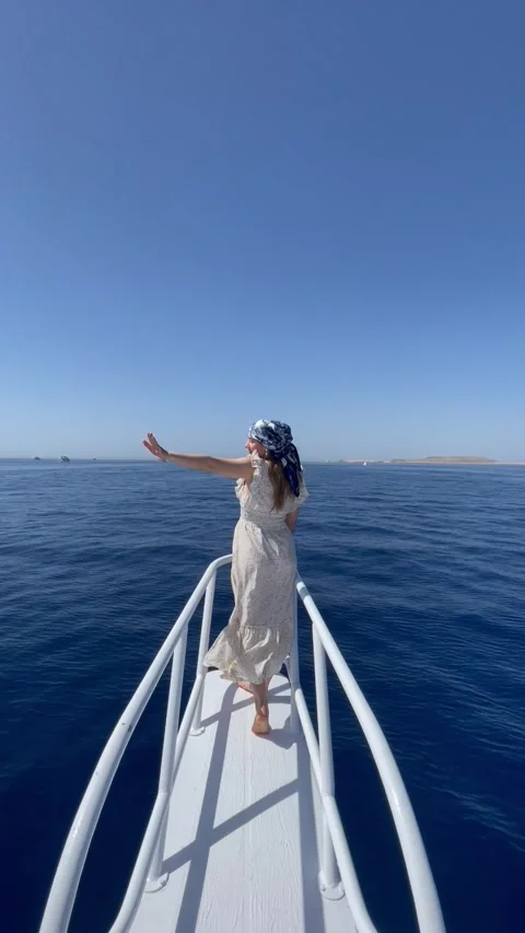 Vertical screen woman in a light summer dress stands at the bow of a boat lookin Stock Footage 317086581