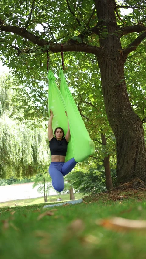 Vertical screen Woman practices aero yoga in a green hammock suspended from a tr Stock Footage 313378790