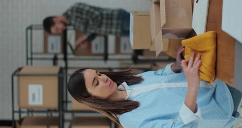 Vertical screen: A woman worker boxes a yellow jumper in a room with shelves Stock Footage 228676566