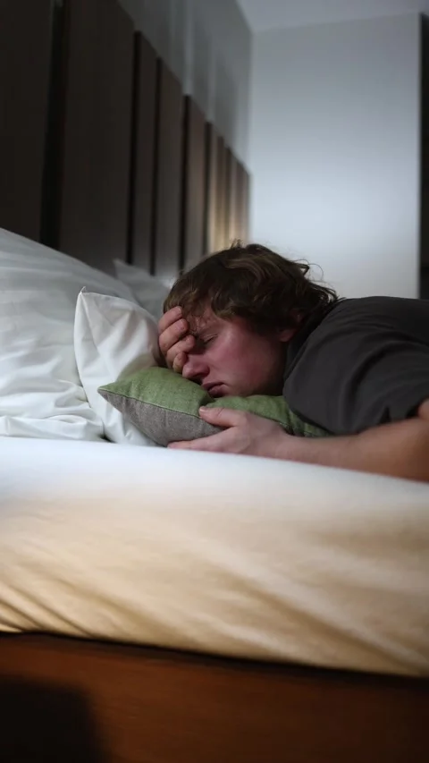 Vertical screen young man in bed holding his head with tired face showing headac Stock Footage 318217617