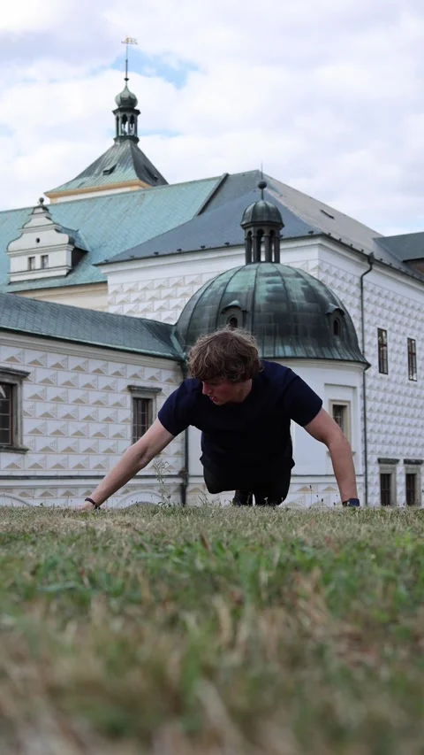 Vertical screen young man doing push ups on grass in front of historic European  Stock Footage 315413784