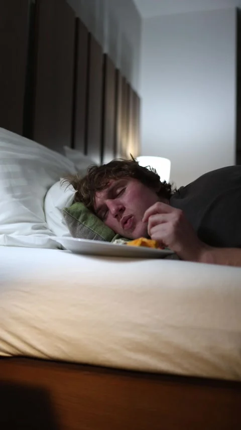 Vertical screen young man falling asleep on bed with food plate beside him late  Stock Footage 318217640