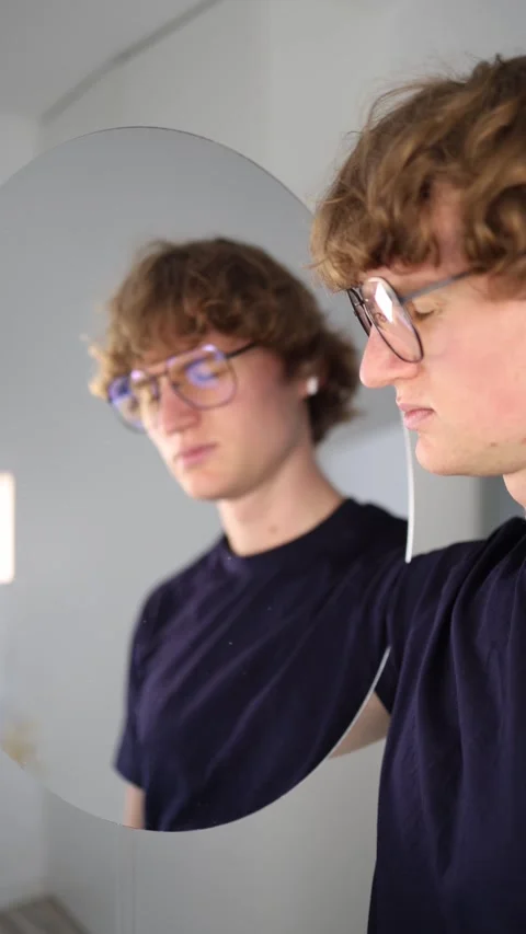 Vertical screen Young man gazes at his reflection with a worried and suspicious  Stock Footage 313268588