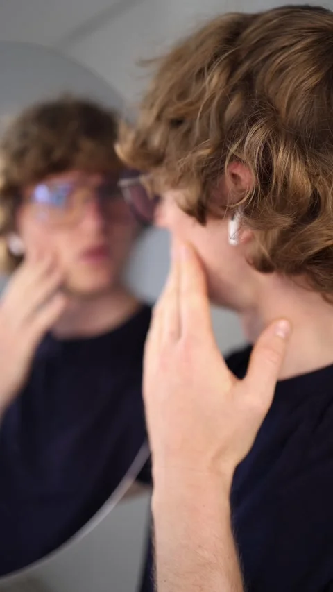 Vertical screen young man gently touches his face while observing his reflection Stock Footage 313268915
