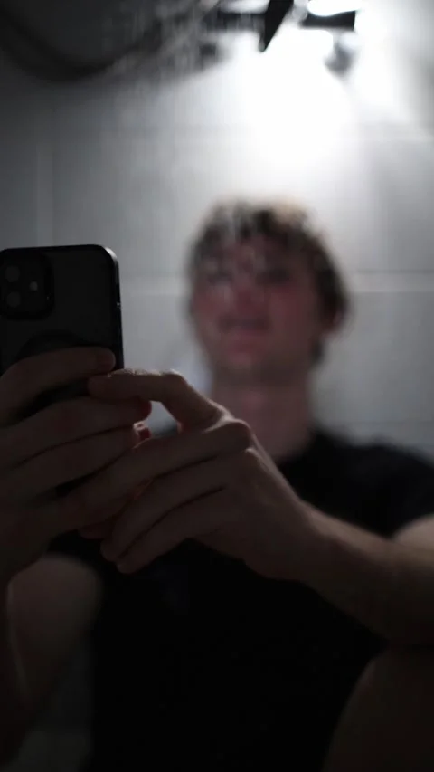 Vertical screen young man holds smartphone under shower staring at screen with f Stock Footage 316066143