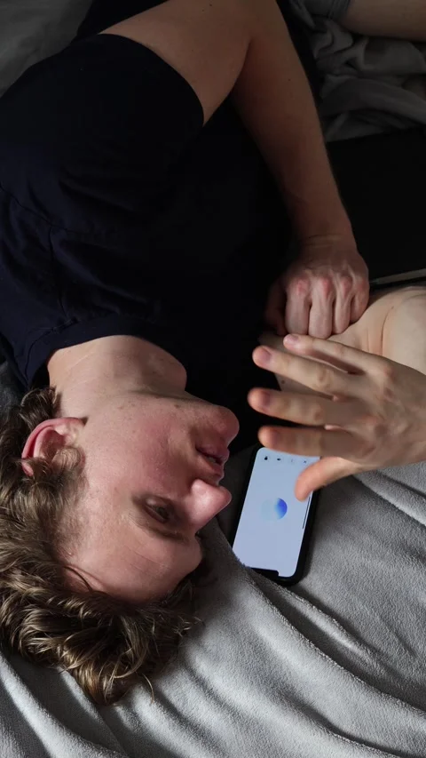 Vertical screen young man lies on bed with smartphone beside him looking tired a Video stock 314979640