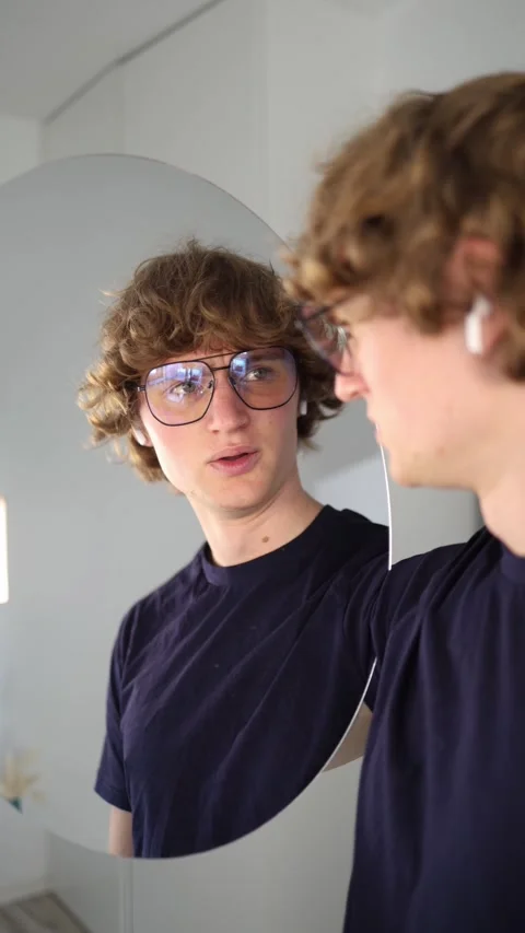 Vertical screen Young man looks at his reflection with surprise and growing affe Stock Footage 313268574