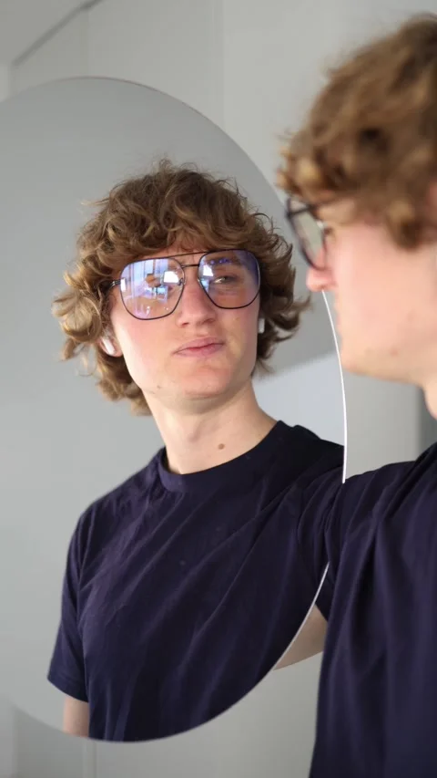 Vertical screen Young man looks at his reflection with subtle skepticism and tig Stock Footage 313268577