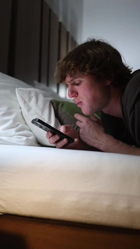 Vertical screen young man lying in bed at night holding smartphone browsing soci Stock Footage 318217590